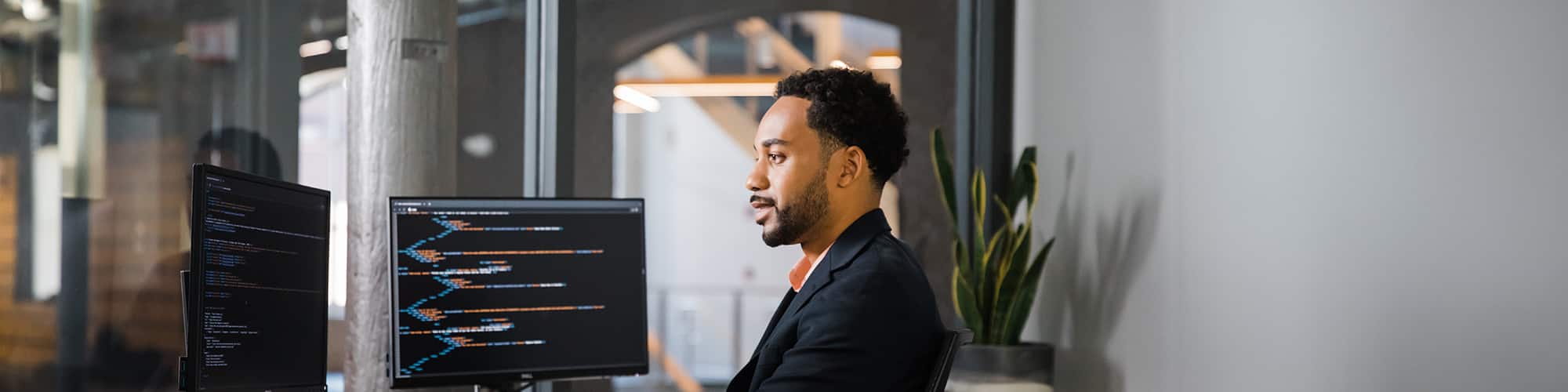 Gary Walker, who earned his SNHU degree in 2021, writing code in an office setting with two monitors