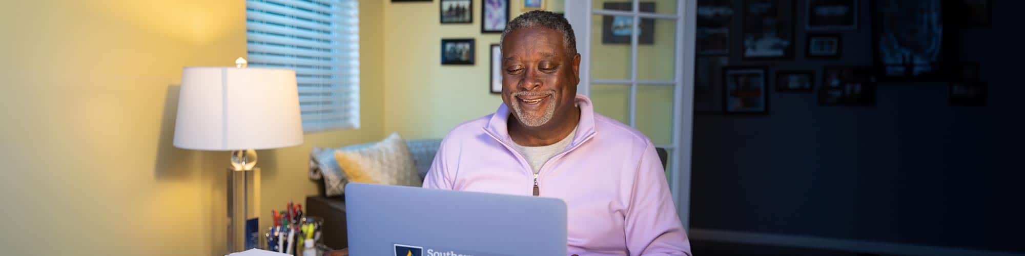 Older man smiling looking down at his laptop in his home office